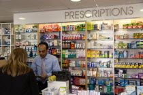 Interior of high street dispensing chemist  with female customer collecting her prescription from the pharmacist assistant behind the counterEuropean Great Britain Northern Europe UK United Kingdom B...