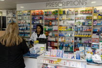 Interior of high street dispensing chemist  with female customer collecting her prescription from the pharmacist behind the counterEuropean Great Britain Northern Europe UK United Kingdom British Isl...