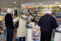 Interior of high street dispensing chemist  with customers collecting prescriptions from the pharmacist assistant behind the counterEuropean Great Britain Northern Europe UK United Kingdom British Is...