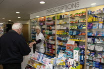 Interior of high street dispensing chemist  with male customer collecting his prescription from the pharmacist assistant behind the counterEuropean Great Britain Northern Europe UK United Kingdom Bri...