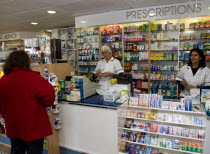 Interior of high street dispensing chemist  with female customer collecting her prescription from the pharmacist assistant behind the counterEuropean Great Britain Northern Europe UK United Kingdom