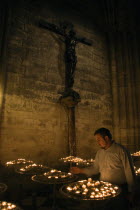 Man lighting votive candles below a cross with Christ crucified in a chapel within the Gothic Cathedral of Notre Dame on the Ile de la CiteFrench Western Europe European