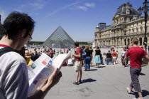 Tourists reading a guide in the square outside the pyramid entrance to the Musee du LouvreFrench Western Europe European