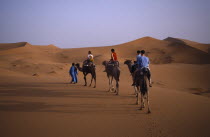 People camel trekking in desert surrounded by sand dunesAfrican al-Magrib Moroccan North Africa