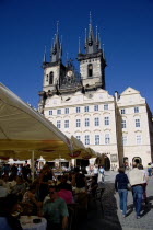 The Old Town Square with the Church of Our Lady before Tyn. Tourists sit at tables under umbrellas outside cafes and restaurants whilst others stroll in the squarePraha Ceska Eastern Europe European...
