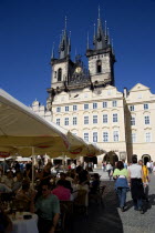 The Old Town Square with the Church of Our Lady before Tyn. Tourists sit at tables under umbrellas outside cafes and restaurants whilst others stroll in the squarePraha Ceska Eastern Europe European...