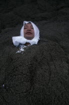 Sunabulo. Hot Sand Bath with a man wearing a white towel wrapped around his head submerged in sand with only his head showing above surfaceAsia Asian Japanese Nihon Nippon