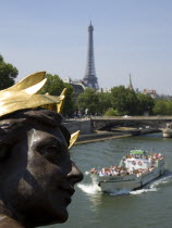 A boat with sightseeing tourists passes below a bronze statue of a woman on the Pont Alexandre III bridge across the River Seine with the Eiffel Tower in the distanceEuropean French Western Europe