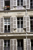 Apartment windows with shutters. An open window has box with red and pink geraniumsEuropean French Western Europe