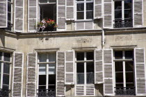 Apartment windows with shutters. An open window has box with red and pink geraniumsEuropean French Western Europe