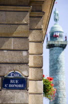 Street sign for Rue St Honore on a wall beside a window box with red geraniums and the statue of Napoleon in Place Vendome on the top of a column modelled on Trajans column in RomeEuropean French Rom...