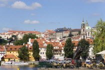 People sitting at tables outside the Smetana Museum on the banks of the Vltava River with the Little Quarter beyondPraha Ceska Eastern Europe European