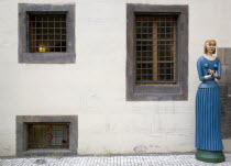 A carved and painted wooden figure of a woman holding a bird in both hands standing on the pavement outside the marionette museum in the Old TownPraha Ceska Eastern Europe European
