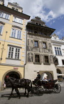 Tourists in a Fiacre horse drawn carriage pass beneath an ornately painted building in the Old Town SquarePraha Ceska Eastern Europe Equestrian European