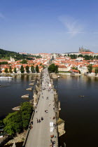 People walking on The Charles Bridge across the Vltava River leading to the Little Quarter. A river cruise boat moves up river to pass under the bridge with Prague Castle and St Vituss Cathedral on th...