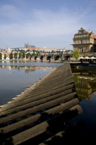 Wooden barrier at the weir on the Vltava River with the Charles Bridge and Prague Castle with St Vituss Cathedral beyond in HradcanyPraha Ceska Eastern Europe European