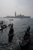Gondolas carrying sighseeing tourists entering the Rio del Palazzo to pass under the Bridge of Sighs with the island of San Giorgio Maggiore and its church of the same name by Palladio beyond