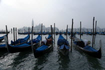 Gondolas moored by Molo San Marco with Palladios church of San Giorgio Maggiore beyond. Two gondoliers prepare their boats on a misty day