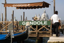 A gondola stand with gondoliers beside Molo San Marco with the Baroque church of Santa Maria della Salute beyond