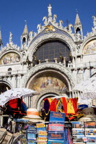 The four bronze Horses of St Mark on the facade of the basilica surrounded by 17th Century mosaics. A stall in the Piazza San Marco in the foreground sells souvenirs