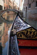 The bow of a gondola approaching a bridge across an empty canal in the San Marco district