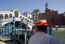 Gondolier wearing a straw boater hat close to his gondola moored beside the tourist crowded Rialto Bridge spanning the Grand Canal