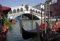 The tourist crowded Rialto Bridge spanning the Grand Canal with gondolas moored in the foreground