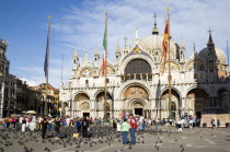 Tourists in the Piazza San Marco feeding pigeons with the Basilica of St Mark at the far end of the square