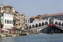 The Rialto Bridge  crowded with tourists  spanning the Grand Canal with boats moored by the quayside and a gondola crossing the canal