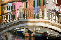 A bridge over a canal with moored boats beside colourful houses on the lagoon island of Burano