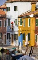 Colourful houses and a religious shrine beside a canal with moored boats on the lagoon island of Burano.