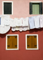 Burano Island in the lagoon. Washing hanging from a line on a colourful building between four shuttered windows