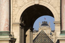The French Tricolour flag flying from the centre of the Sully wing of the Musee du Louvre seen through the Arc de Triomph du Carrousel with the museum Pyramid entrance between them.Center European We...