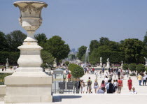 Stone urn planter at the entrance to the Jardin des Tuileries with tourists walking through the gardens towrds the Champs ElyseesEuropean French Western Europe