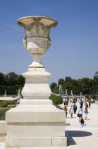 Stone urn planter at the entrance to the Jardin des Tuileries with tourists walking through the gardens towrds the Champs ElyseesEuropean French Western Europe
