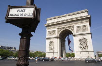Tourists at the base of the Arc de Triomphe in Place Charles de Gaulle with traffic going around it. A large French Triclour flag hangs in the central arch of the ArcEuropean Western Europe
