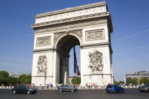 Tourists at the base of the Arc de Triomphe in Place Charles de Gaulle with traffic going around it. A large French Triclour flag hangs in the central arch of the ArcEuropean Western Europe