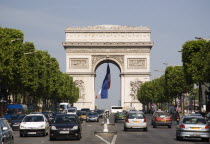 Road traffic on the Champs Elysees leading to the Arc de Triomphe in Place Charles de Gaulle. A large French Triclour flag hangs in the central arch of the ArcEuropean Western Europe