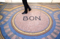 Pedestrian walk across a mosaic on the pavement with the word Bon at the centreCenter European French Western Europe