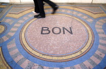 Pedestrians walk across a mosaic on the pavement with the word Bon at the centreCenter European French Western Europe