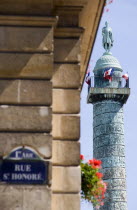 Road sign on a corner wall for Rue St Honore in the premier Arrondissement with a windowbox of red geraniums and the monument to Napoleon in Place Vendome beyondEuropean French Western Europe