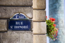 Road sign on a corner wall for Rue St Honore in the premier Arrondissement with a windowbox of red geraniums and the monument to Napoleon in Place Vendome beyondEuropean French Western Europe