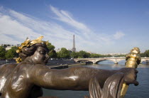 Bronze female figure holding a flame on the Pont Alexandre III bridge across the River Seine below with the Eiffel Tower beyondEuropean French Western Europe