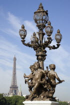 Ornate bronze lamp-post with cherubs on the Pont Alexandre III bridge with the Eiffel Tower beyondEuropean French Western Europe