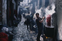 Street in the wool dyeing souk with man in foreground lifting skein of yarn from vat of dye.