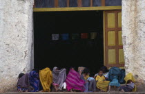 Children sitting in doorway of building wrapped in colourful blankets as protection against the cold.