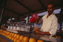 Dejemma el Fna. A man ouring a glass of orange juice. Rows of oranges and glassess in the bar.