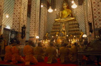 Monks pray  kneeling down in front of large golden Buddha at Wat Arun. The Temple of Dawn.Asian Prathet Thai Raja Anachakra Thai Religion Siam Southeast Asia Religious Siamese Asian Prathet Thai Raj...