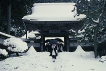 Mount Koya-san.  Venerated Shingon-Buddhist site.  Novice monks walking through gateway of temple complex in heavy snow.Asia Asian Japanese Nihon Nippon Religion Religious Asia Asian Japanese Nihon...