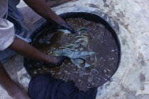 Cropped view of worker and indigo dye pit.  To achieve a  dark colour requires repeated immersions. Color African Nigerian Western Africa  Color African Nigerian Western Africa